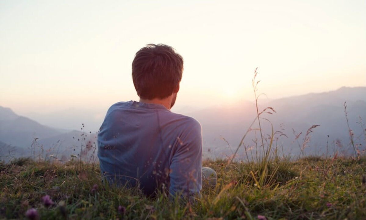 muž ležiaci v tráve sa kochá výhľadom na krajinu