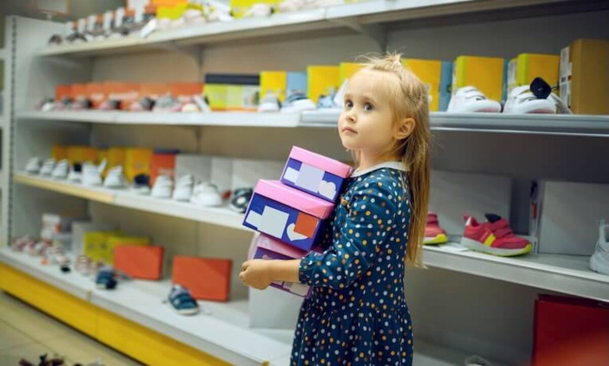 dievčatko v predajni s obuvou nesie tri škatule s topánkami