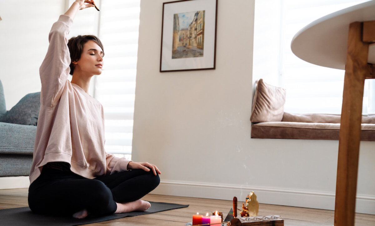žena praktikujúca dychové cvičenia v tureckom sede v príjemnej atmosfére so sviečkami