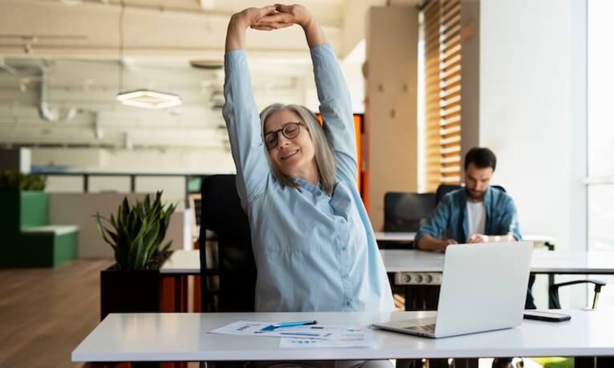 žena pracujúca na notebooku si naťahuje chrbát na stoličke
