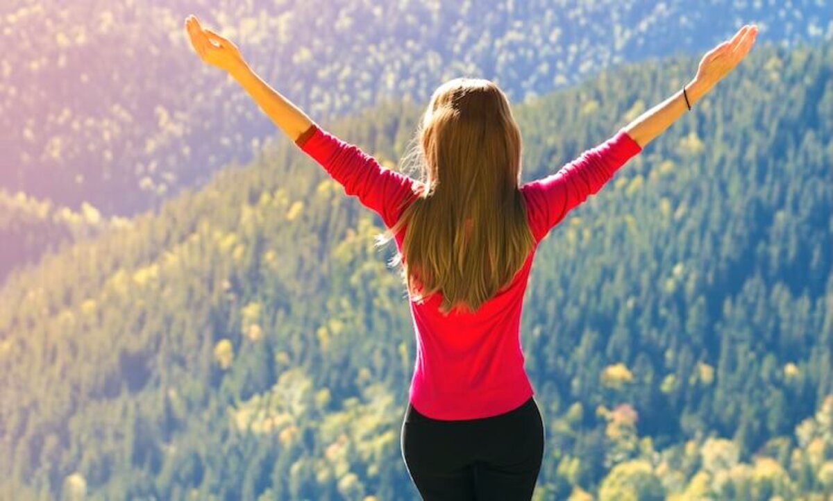 žena s rozpaženými rukami sa zvysoka díva na stromy 
