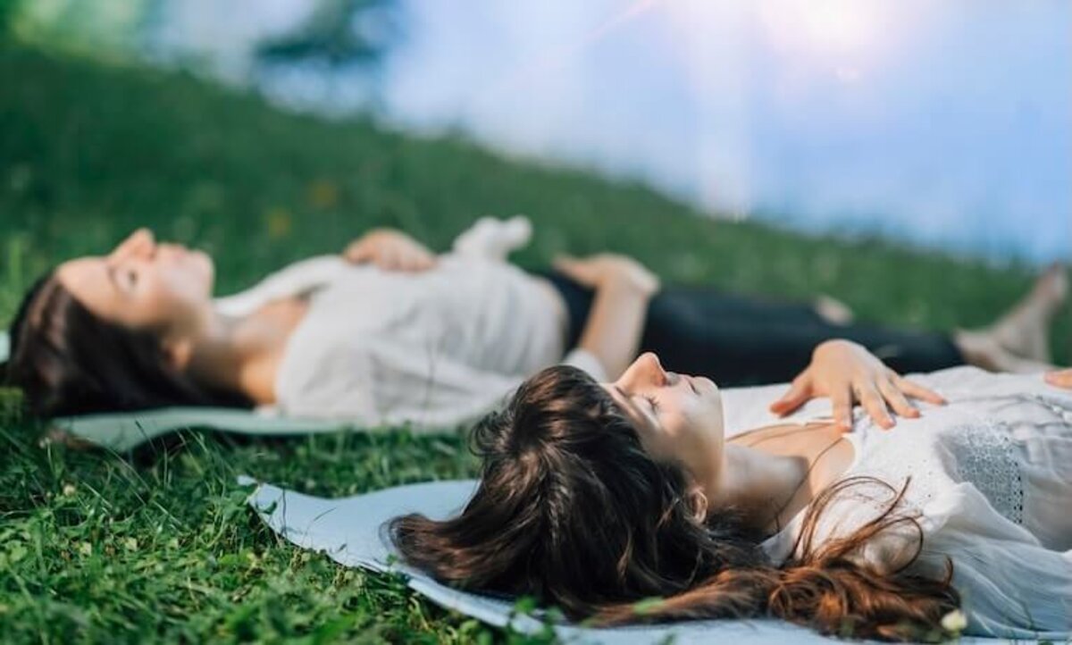 dve ležiace ženy na karimatkách v tráve praktikujú dychové cvičenia