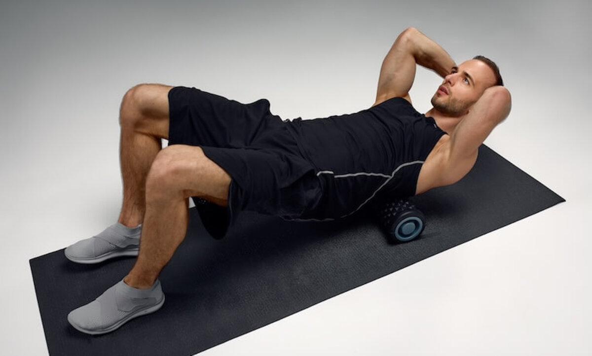 muž masírujúci si chrbát na penovom valci v ľahu na chrbte