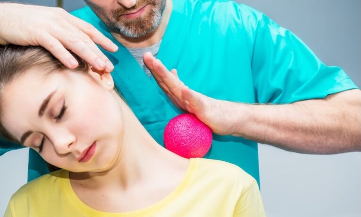 fyzioterapeut masíruje loptičkou hornú časť chrbta mladej ženy