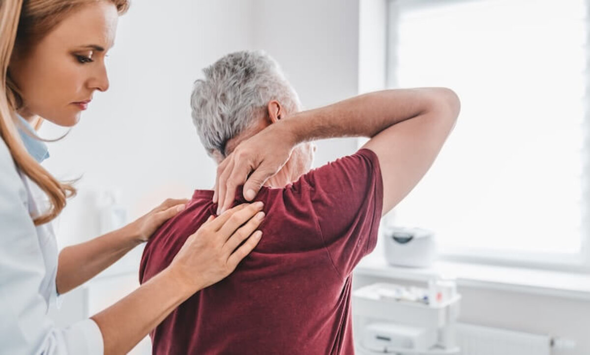 lekárka vyšetruje muža s bolesťou v hornej časti chrbta