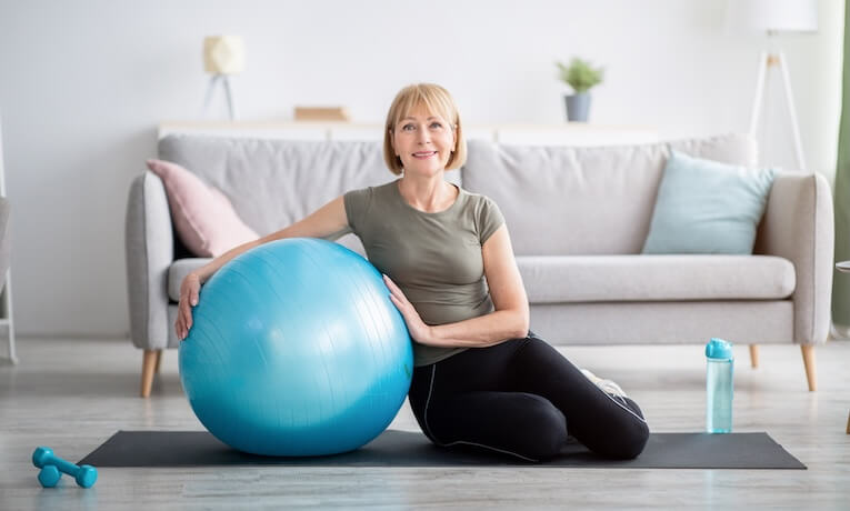 žena v strednom veku s gymnastickou loptou na karimatke