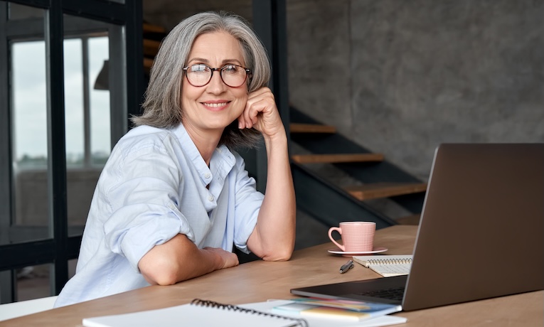 žena v strednom veku sediaca za stolom s notebookom