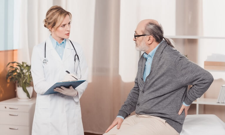 lekárka v rozhovore so starším pacientom s bolesťou v krížoch