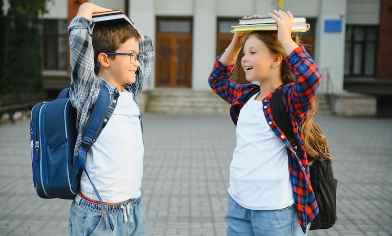 školáci dievča a chlapec s taškami na chrbtoch a knižkami na hlavách