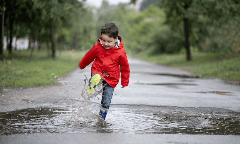 chlapec v gumákoch skáče v mláke