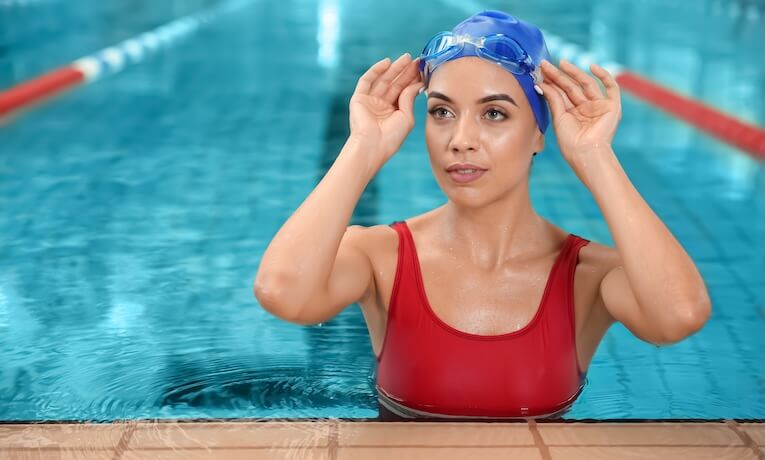 mladá plavkyňa si nasadzuje plavecké okuliare pri kraji bazéna