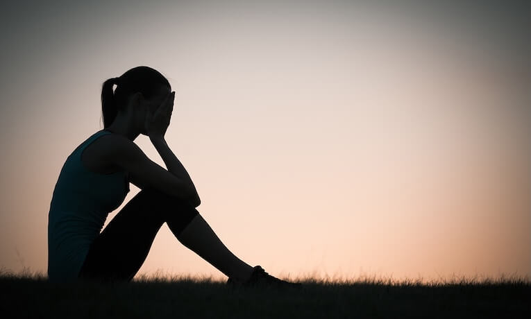 obrys sediacej ženy s rukami pritlačenými na tvár